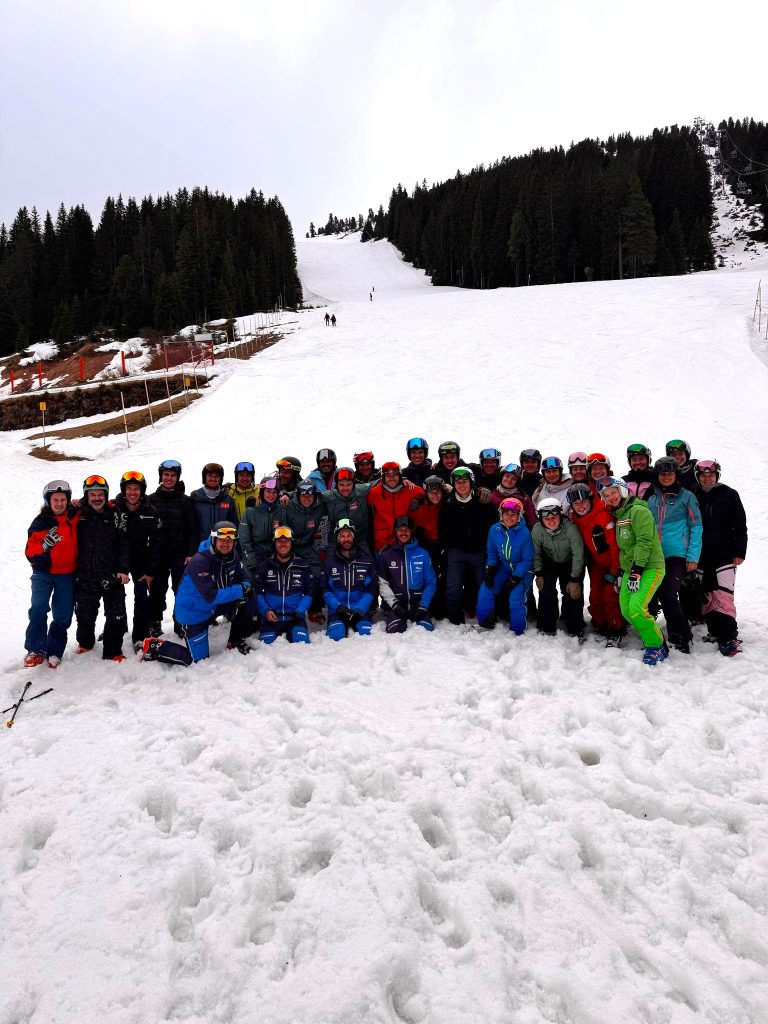 Gruppe fröhlicher Skifahrer vor verschneiter Berglandschaft.