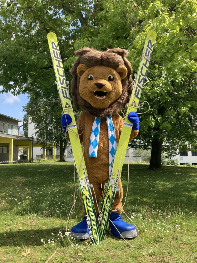 Maskottchen Schorski stehend mit Ski in der Hand