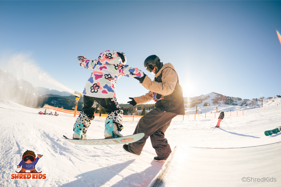 Snowboard Kind fährt über Rampe mit Hilfe von Coach