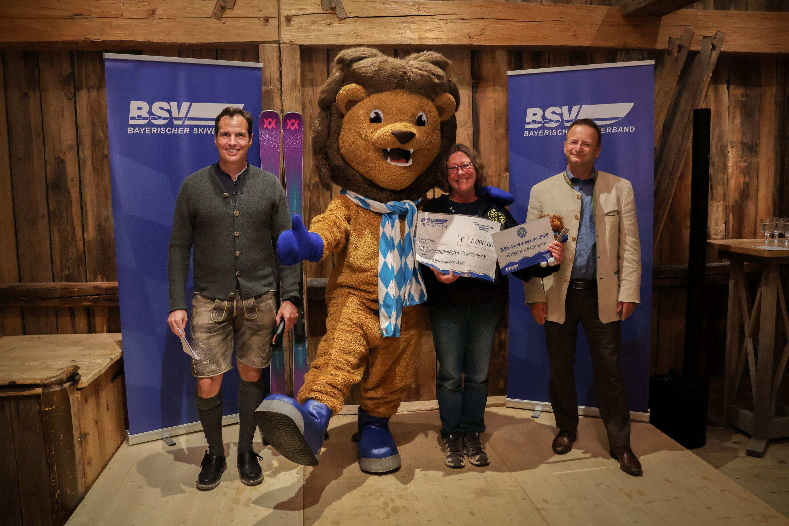 Gruppenbild mit drei Personen und einem Maskottchen bei Preisübergabe