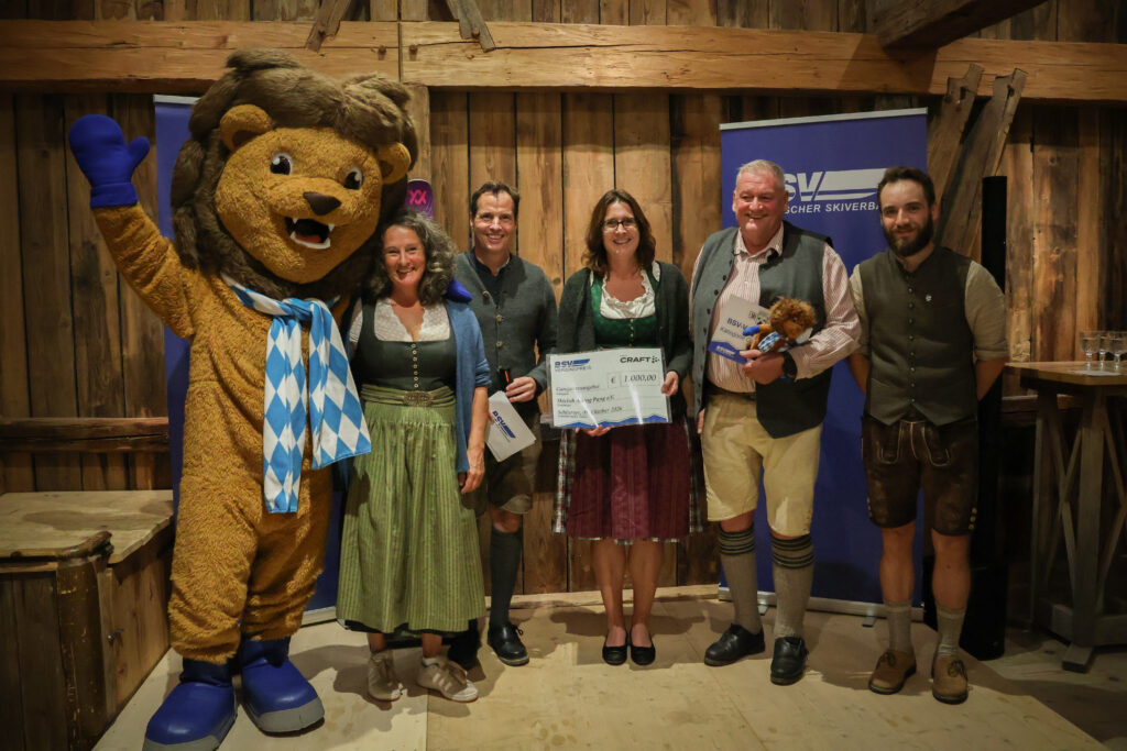 Gruppenbild mit fünf Personen und einem Maskottchen bei Preisübergabe