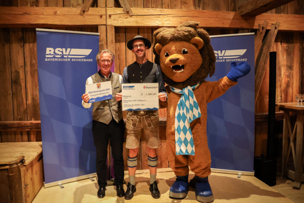 Gruppenbild mit zwei Personen und einem Maskottchen bei Preisübergabe