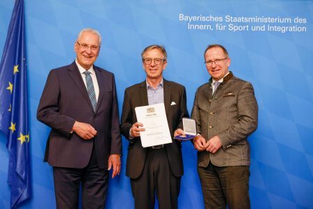 Foto von 3 Personen bei Überreichen einer Ehrung