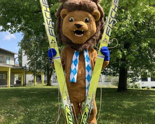 Maskottchen Schorski stehend mit Ski in der Hand