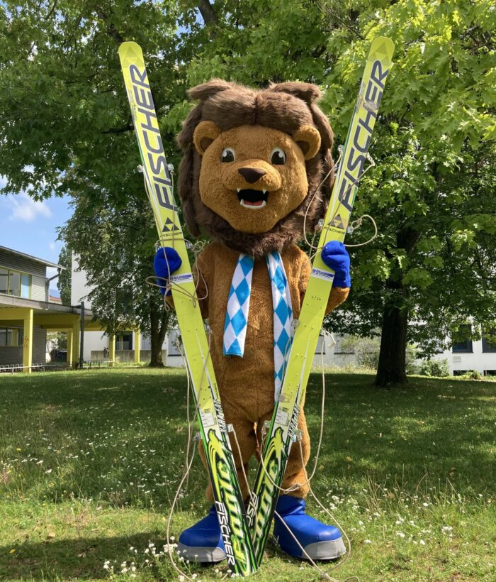 Maskottchen Schorski stehend mit Ski in der Hand
