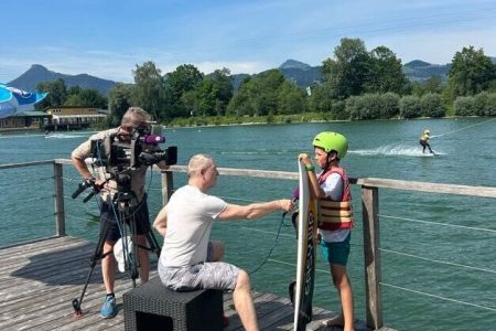 Interview Team mit Kamera und Microfon interviewt Wakeboarder vor Wasserskianlage