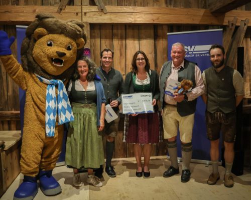 Gruppenbild mit f&uuml;nf Personen und einem Maskottchen bei Preis&uuml;bergabe
