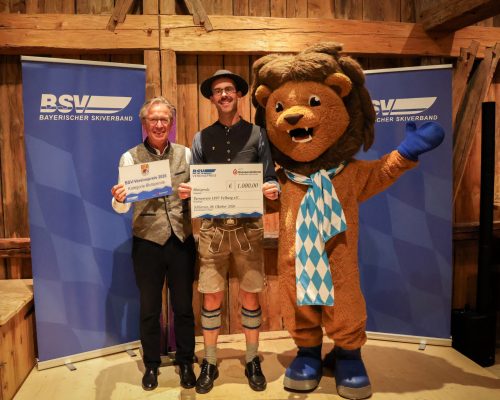 Gruppenbild mit zwei Personen und einem Maskottchen bei Preis&uuml;bergabe